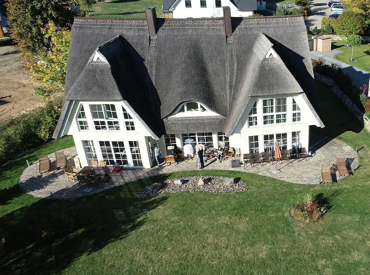Una casa grande de dos pisos con un techo inclinado, un porche con mobiliario exterior y un jardín bien cuidado.