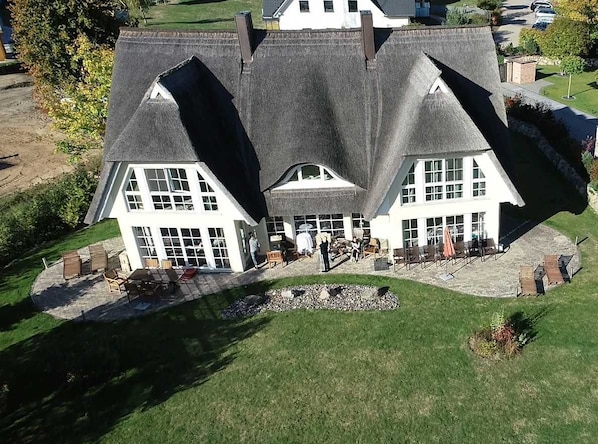 A large, two-story house with a steeply pitched roof, a front porch with outdoor seating, and a well-maintained lawn.