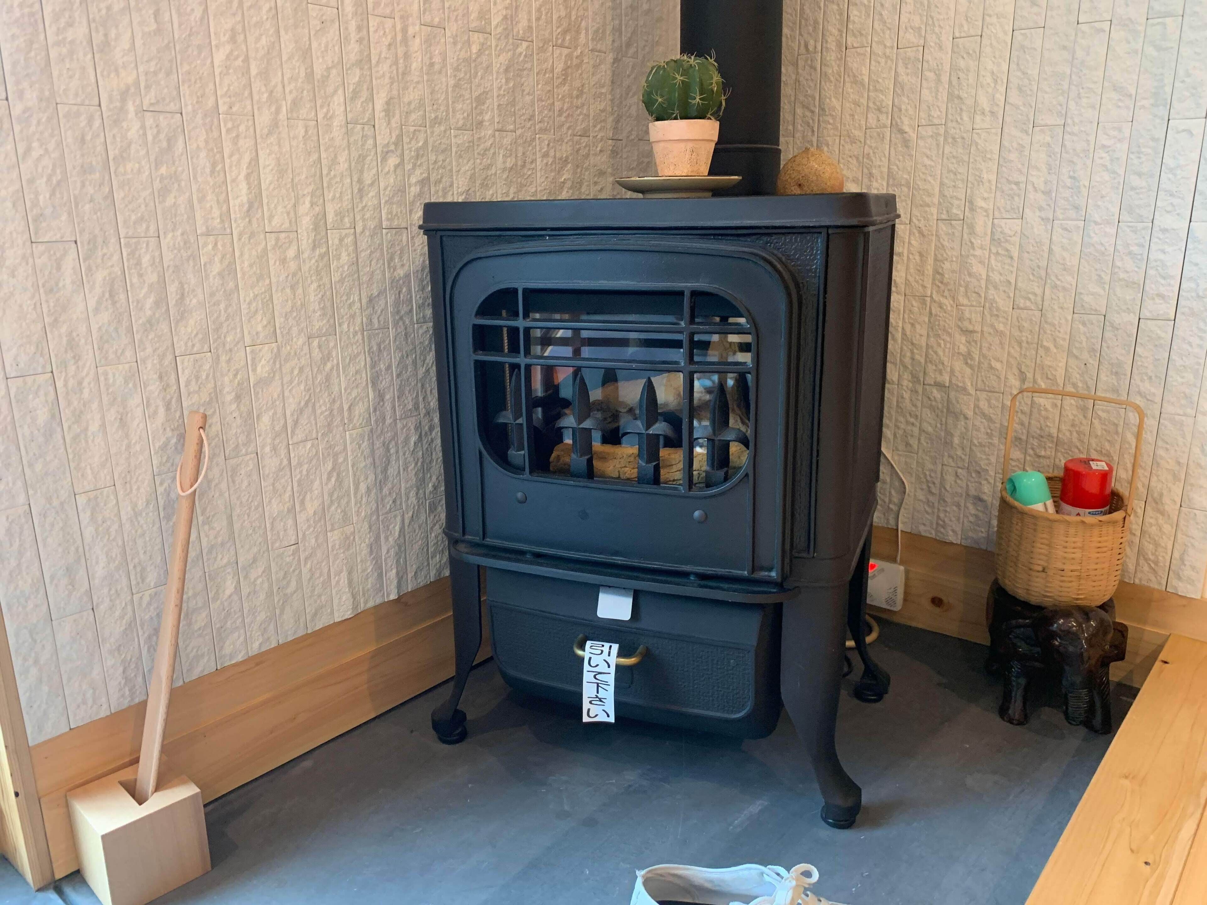 A black wood-burning stove with a tag, a broom, a cactus, and a basket with items on a wooden floor.