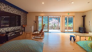 A spacious living room with a large TV, wooden flooring, a rocking chair, and a view of the outdoors through glass doors. - Ukiha Kojio no Akari (Ukiha)