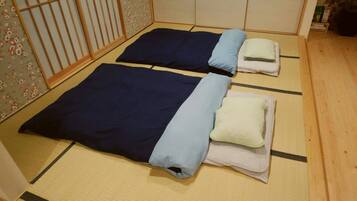 Two single beds with blue and white bedding in a room with tatami flooring and a wooden door.