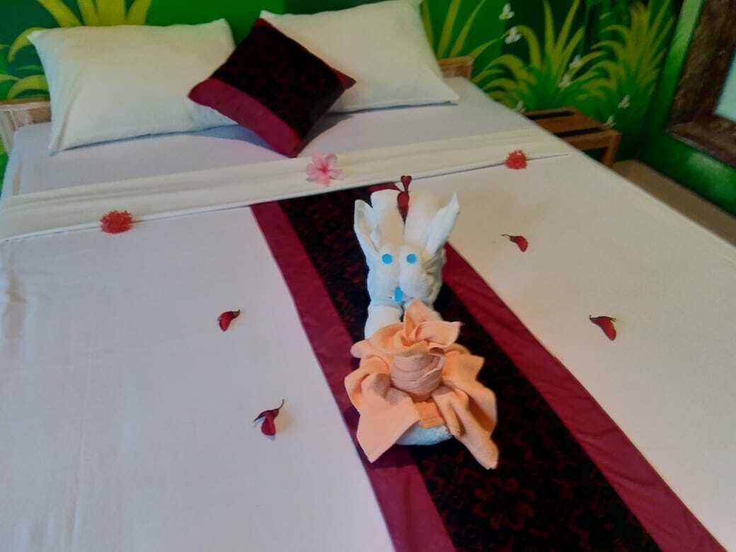 Una cama bien hecha con un adorno central de toallas, una colcha a rayas rojas y blancas, y un cojín con diseño floral.