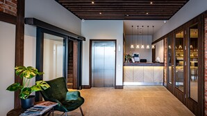 Un hall d’entrée moderne avec un comptoir d’accueil, un fauteuil vert, une plante en pot et un ascenseur.