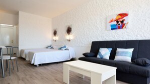 Una habitación de hotel moderna con dos camas individuales, un sofá negro, una mesa de centro blanca y un pequeño escritorio con sillas.