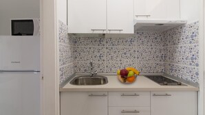 Una cocina compacta con armarios blancos, un lavamanos de acero inoxidable y un frutero sobre la encimera.