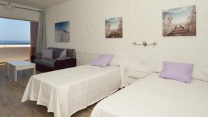 Habitación de hotel con dos camas individuales, un sofá, una mesita pequeña y vistas a la playa.