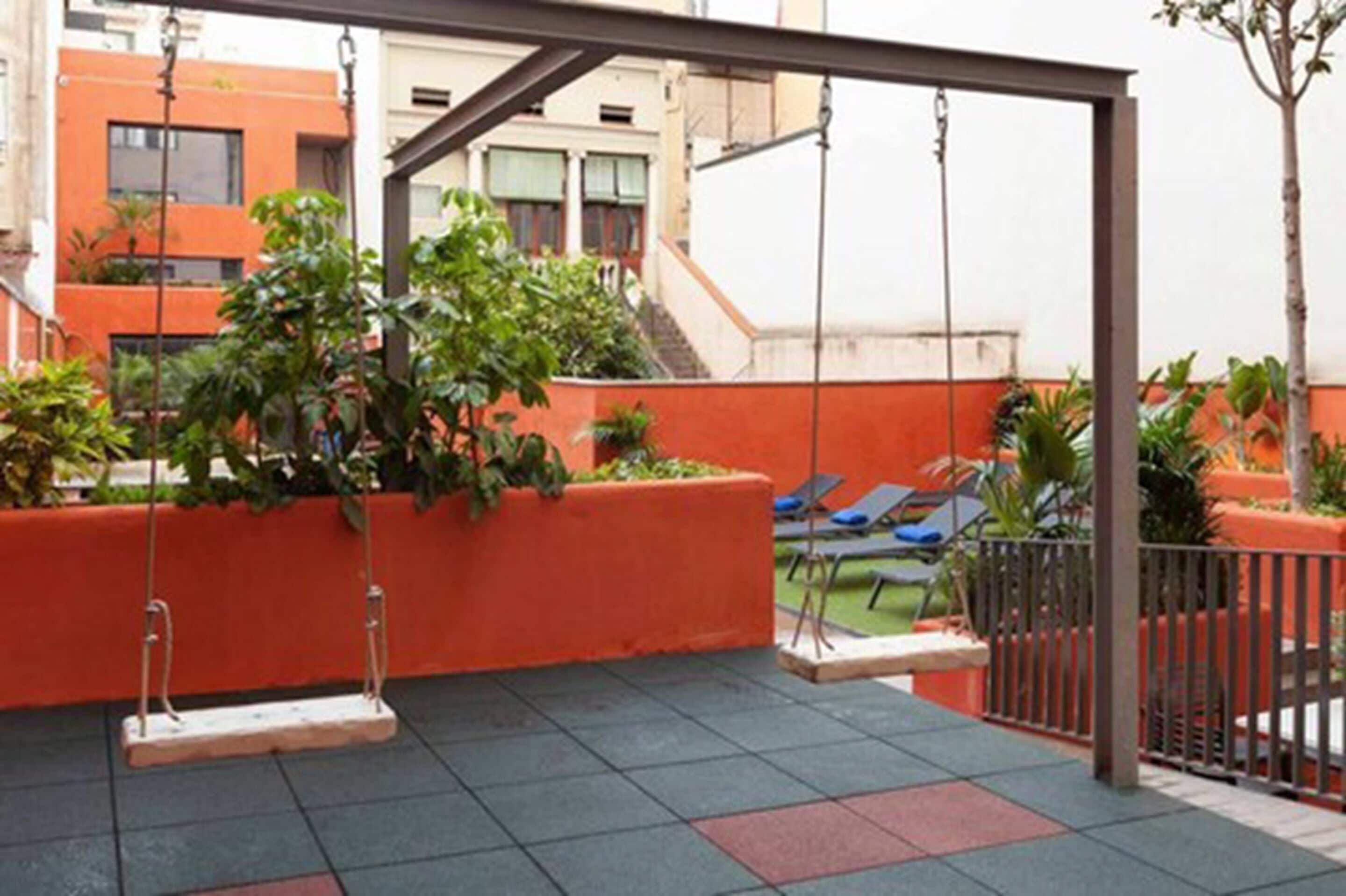 A rooftop patio with a swing set, lounge chairs, and potted plants.