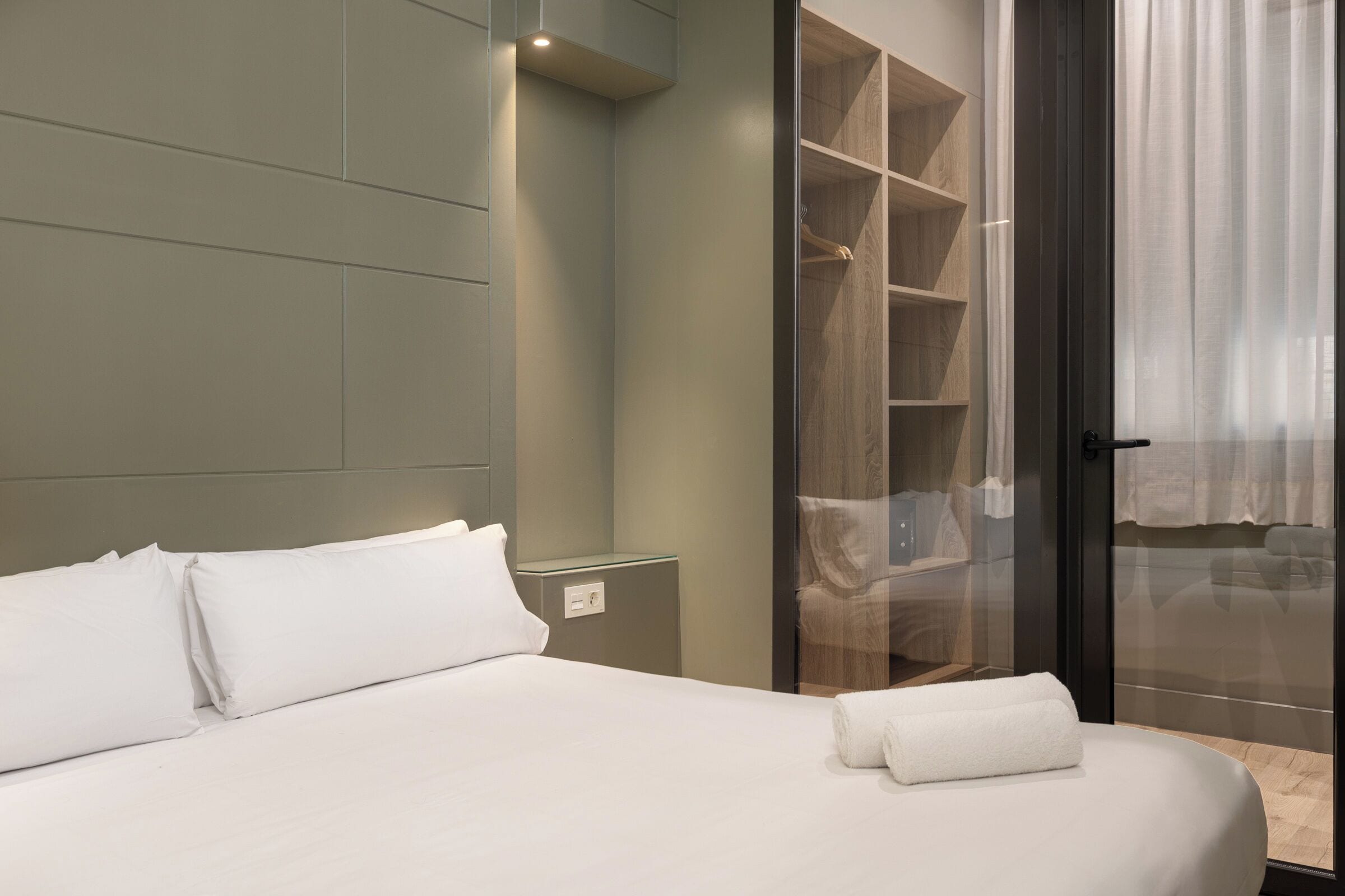 A modern hotel room with a large bed, a walk-in closet, and a sliding glass door leading to a balcony.