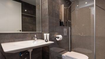 Een moderne badkamer met een wit wastafelmeubel, toilet en een douche met glazen wanden.