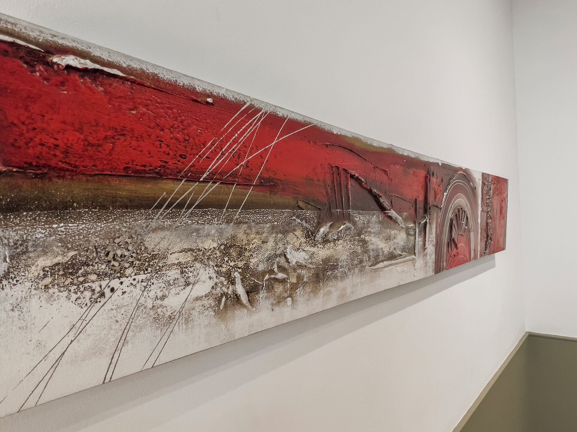 Un cuadro abstracto de gran tamaño con tonos rojos y grises, colgado en una pared blanca.
