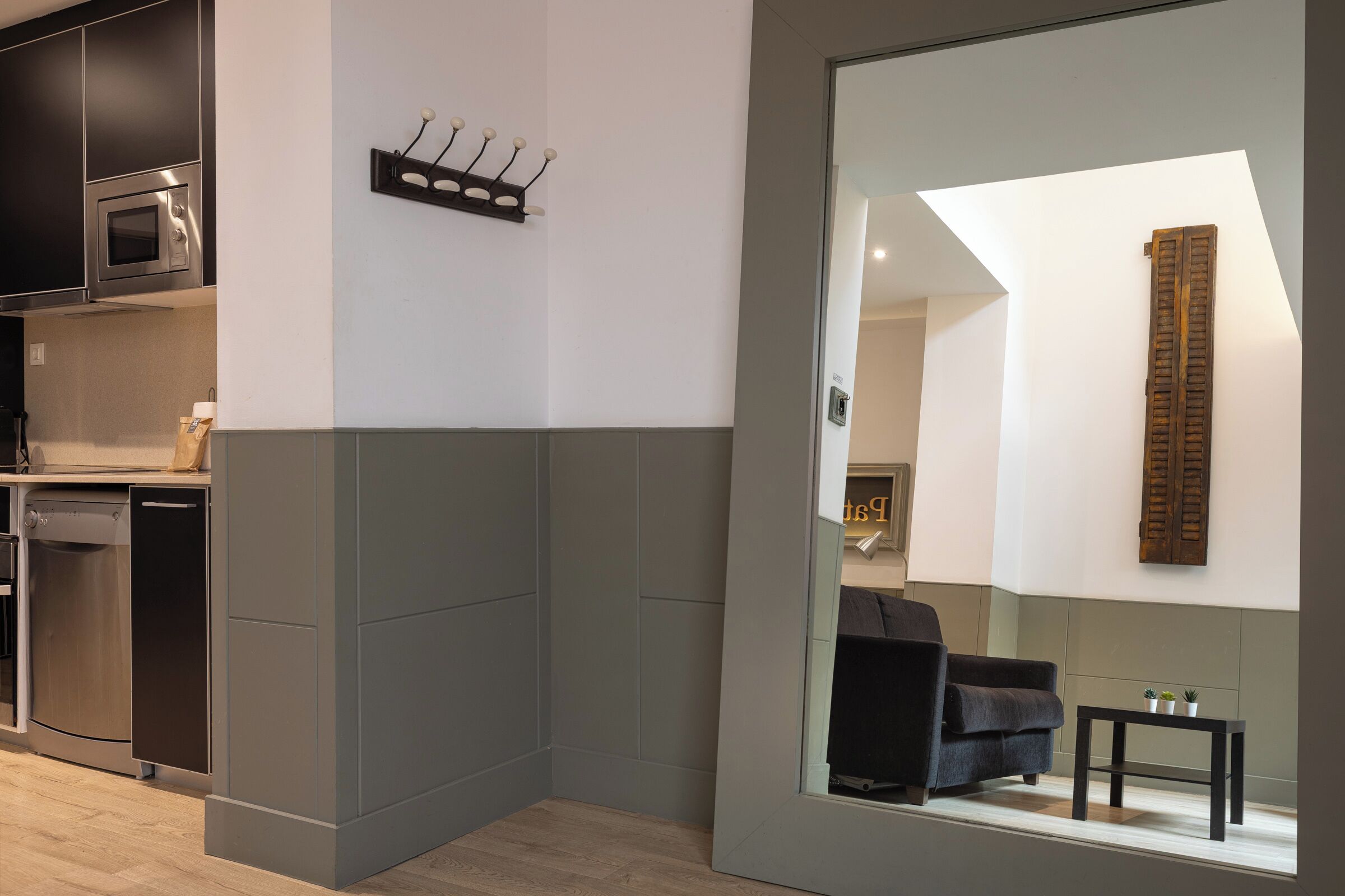 A modern kitchen with built-in appliances, a seating area with a sofa and a small table, and a large mirror reflecting the room.