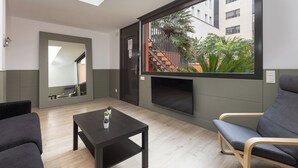 Una sala de estar moderna con un ventanal grande, un televisor de pantalla plana, una mesa de centro oscura y un sofá gris.