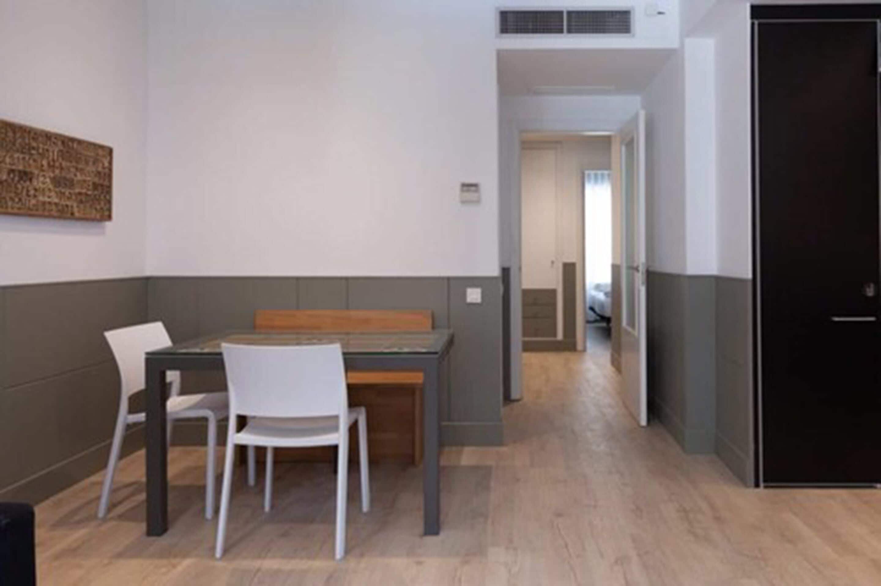 Un comedor moderno con una mesa de madera y sillas blancas, una puerta negra y un pasillo que conduce a otra habitación.