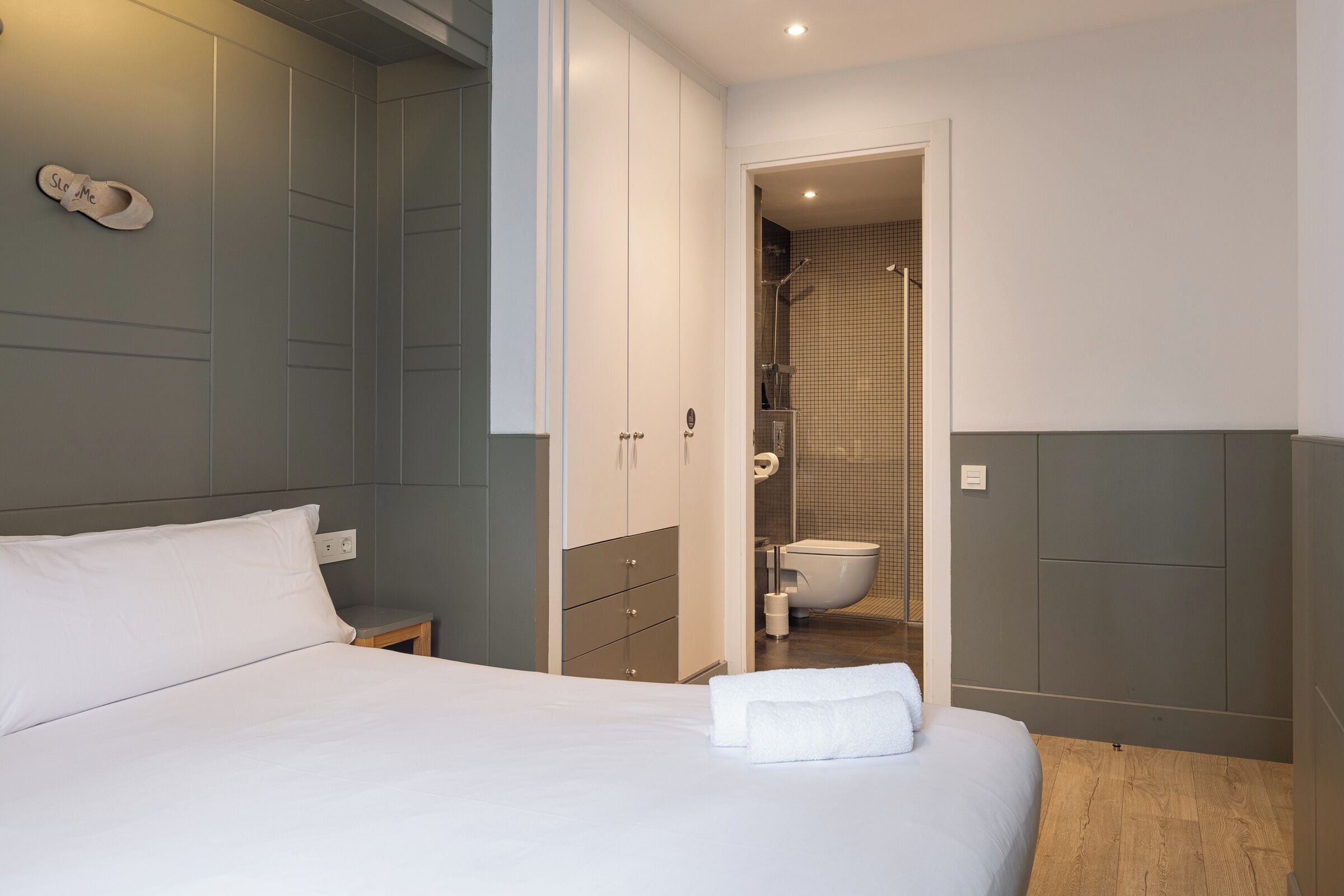A hotel room with a bed, a nightstand, a wardrobe, and a bathroom visible through an open door.