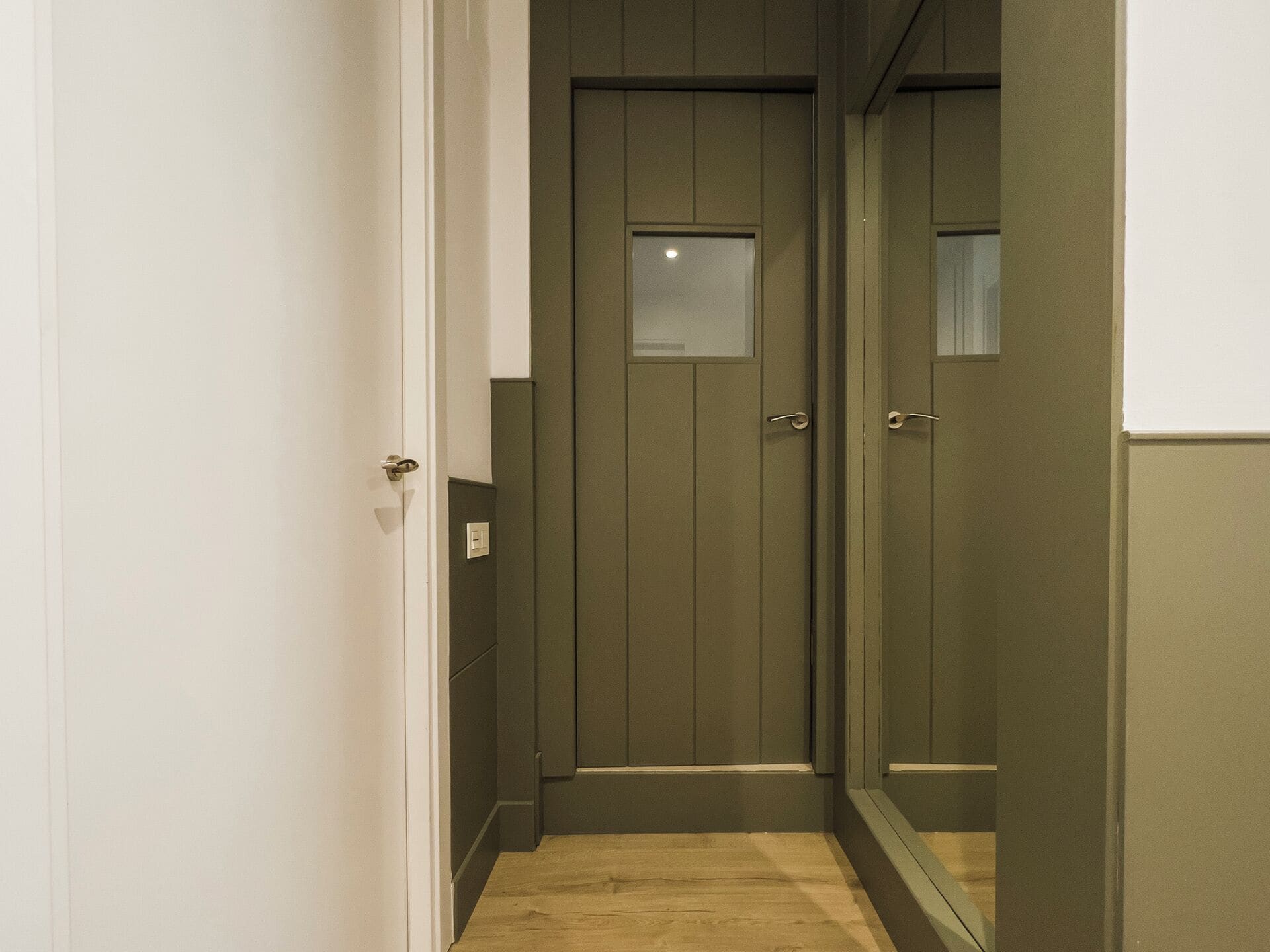 A narrow hallway with a wooden door and a mirror on the right.