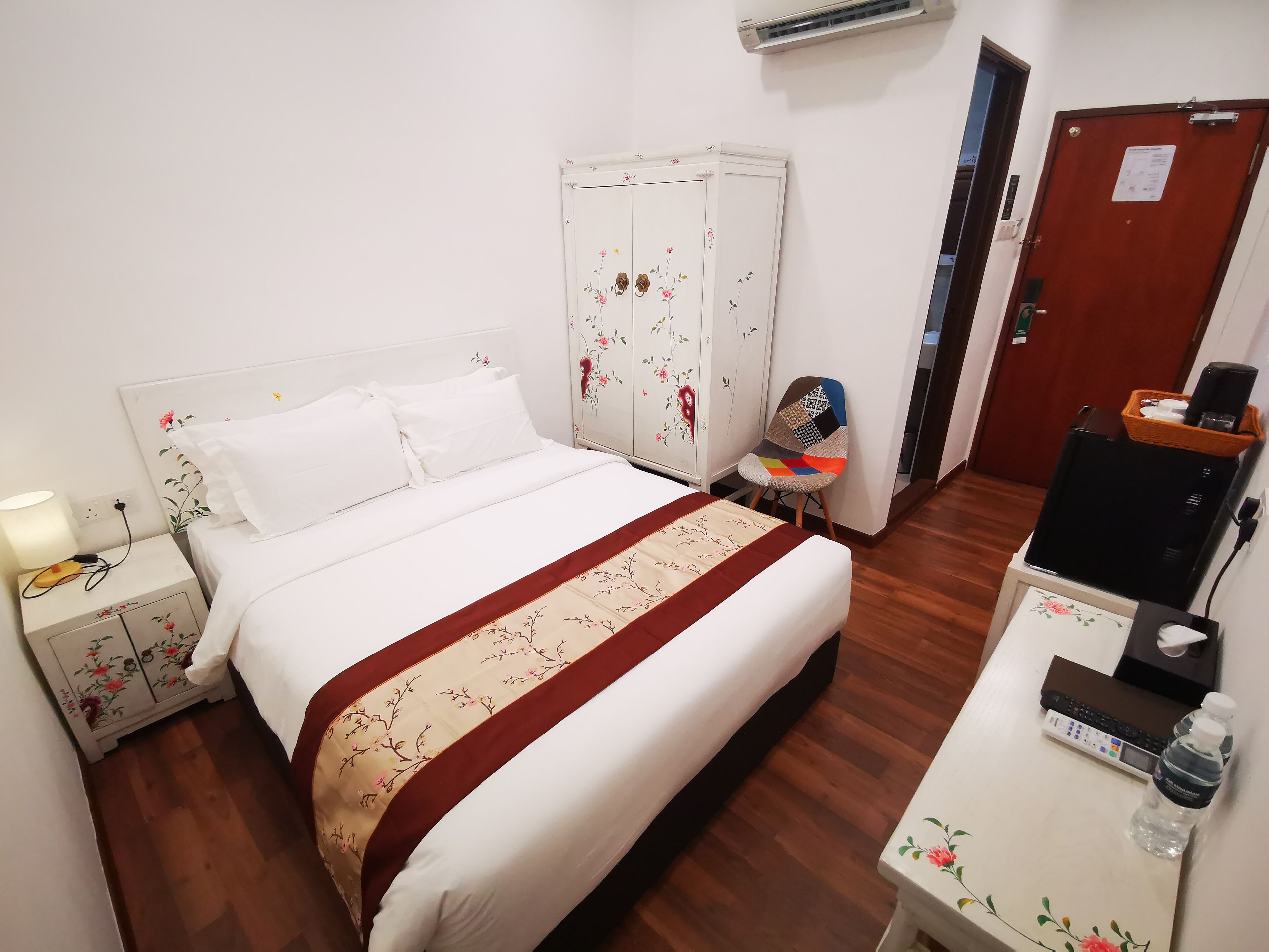A hotel room with a bed, a desk with a computer, a chair, an air conditioner, and a wardrobe.