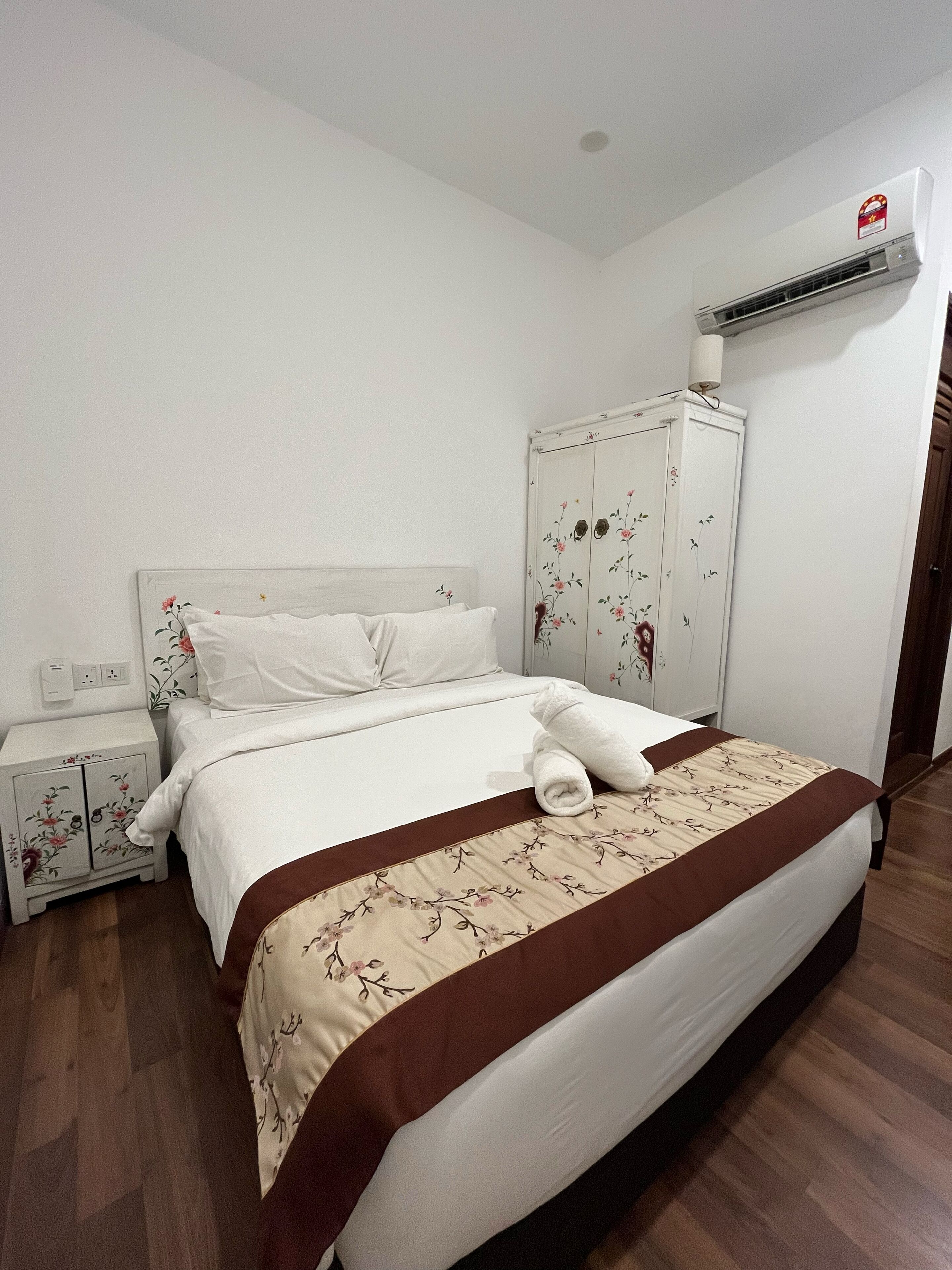 Una cama bien hecha con una colcha marrón y blanca de motivos florales, un cabecero blanco y una mesita de noche blanca con estampados florales.