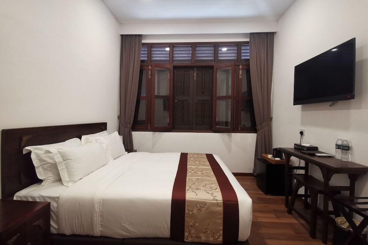 A hotel room with a bed, a desk, a TV, and a window with curtains.