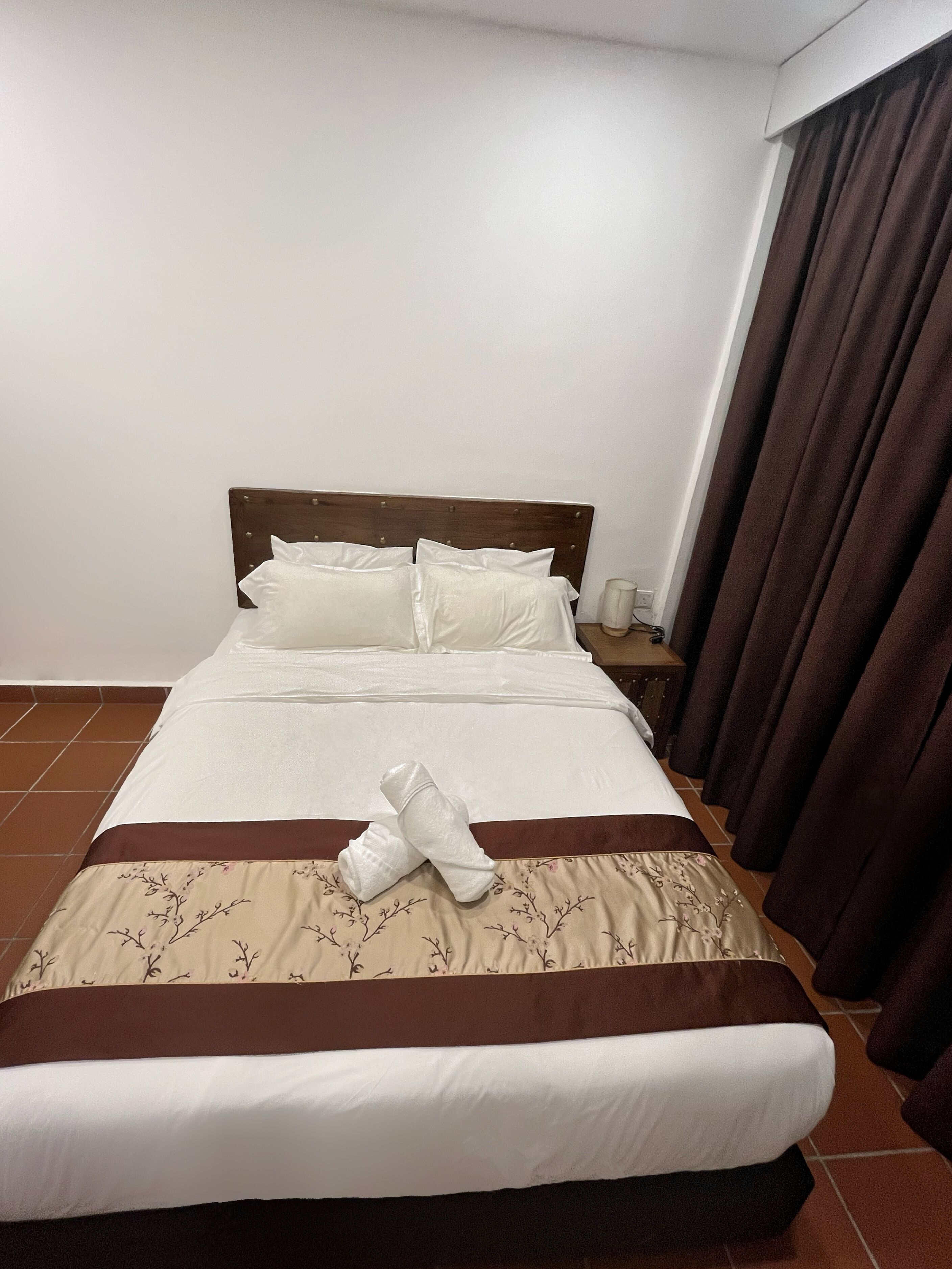 Una cama bien tendida con sábanas blancas, cabecera marrón y edredón estampado con motivos florales.