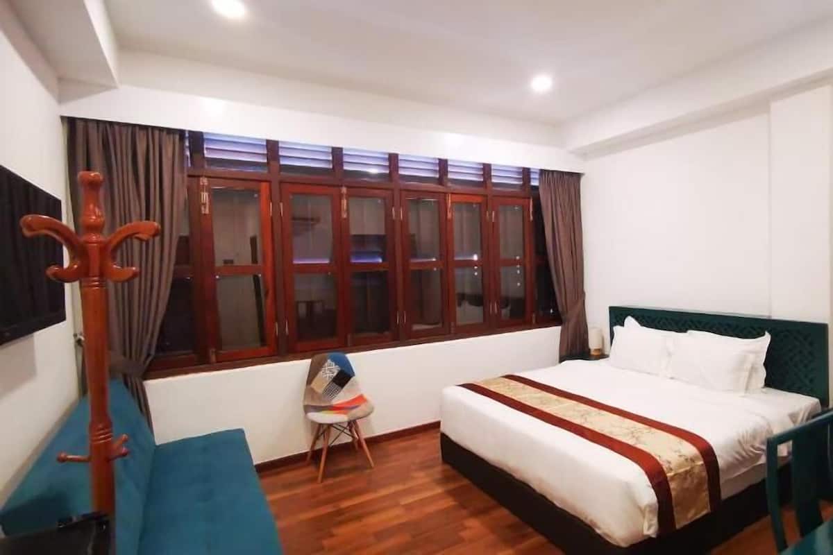 Ein Schlafzimmer mit einem Bett, einem Sessel, einem Schreibtisch, einem Fenster mit Vorhängen und Holzboden.