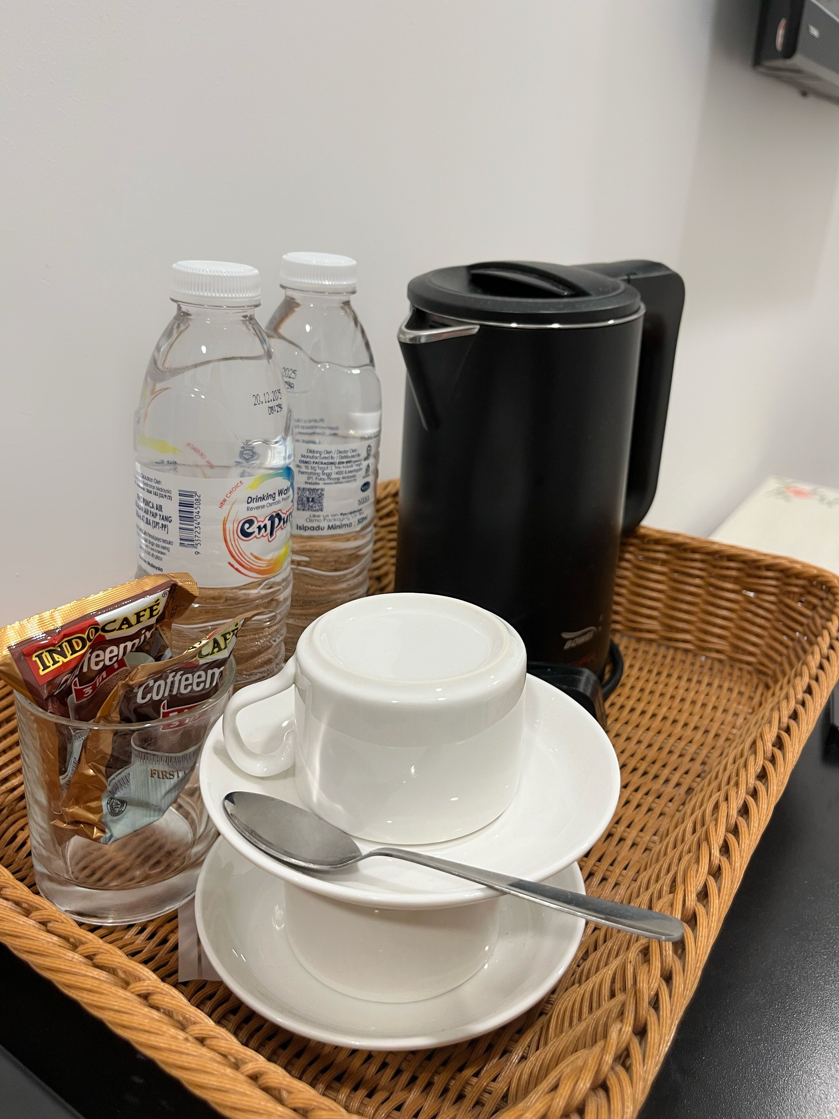 Una bandeja con una taza blanca, una cuchara, dos botellas de agua y un paquete de sobres de café.
