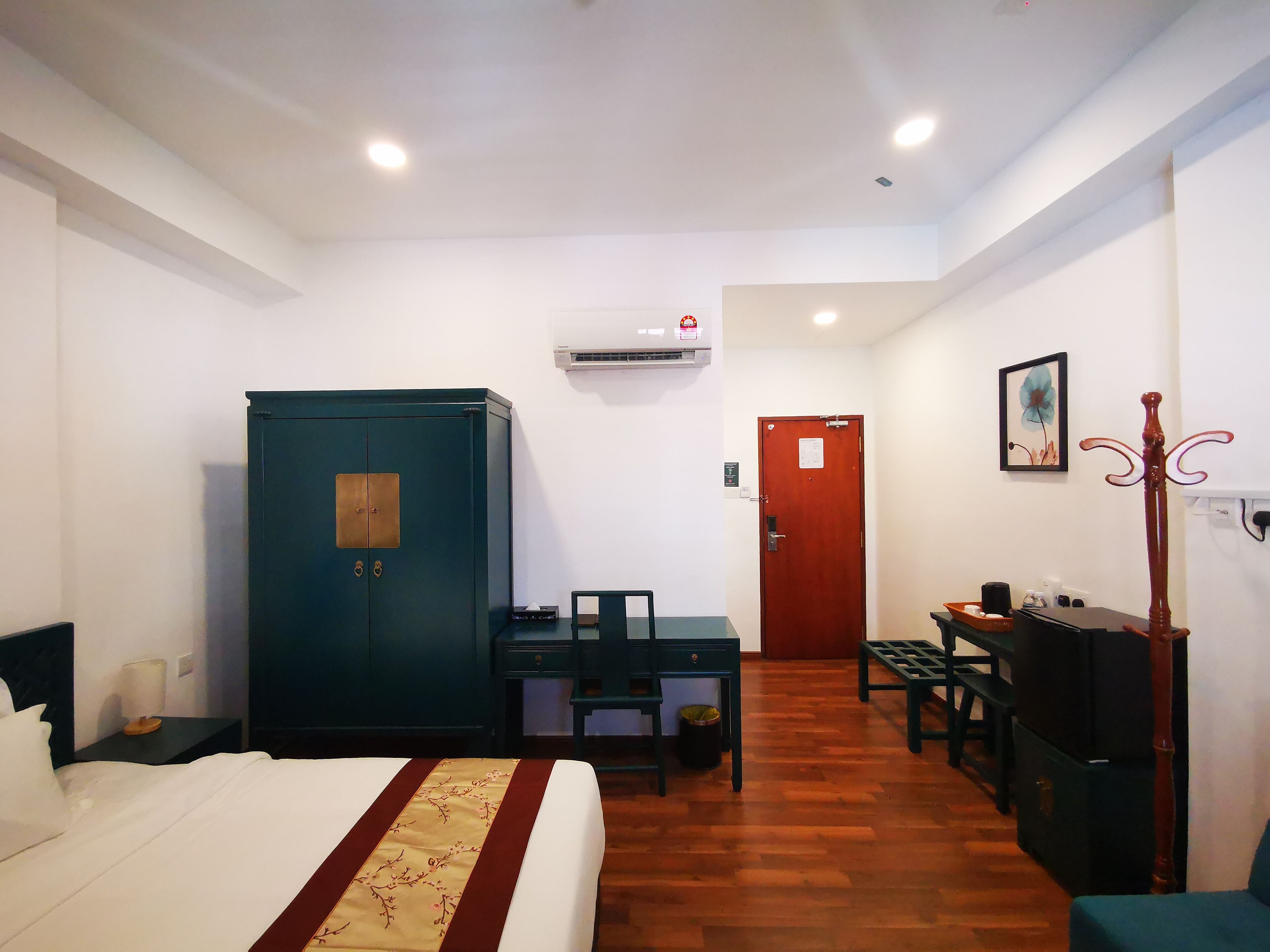 Habitación de hotel con cama, escritorio, silla, armario, televisor y perchero.