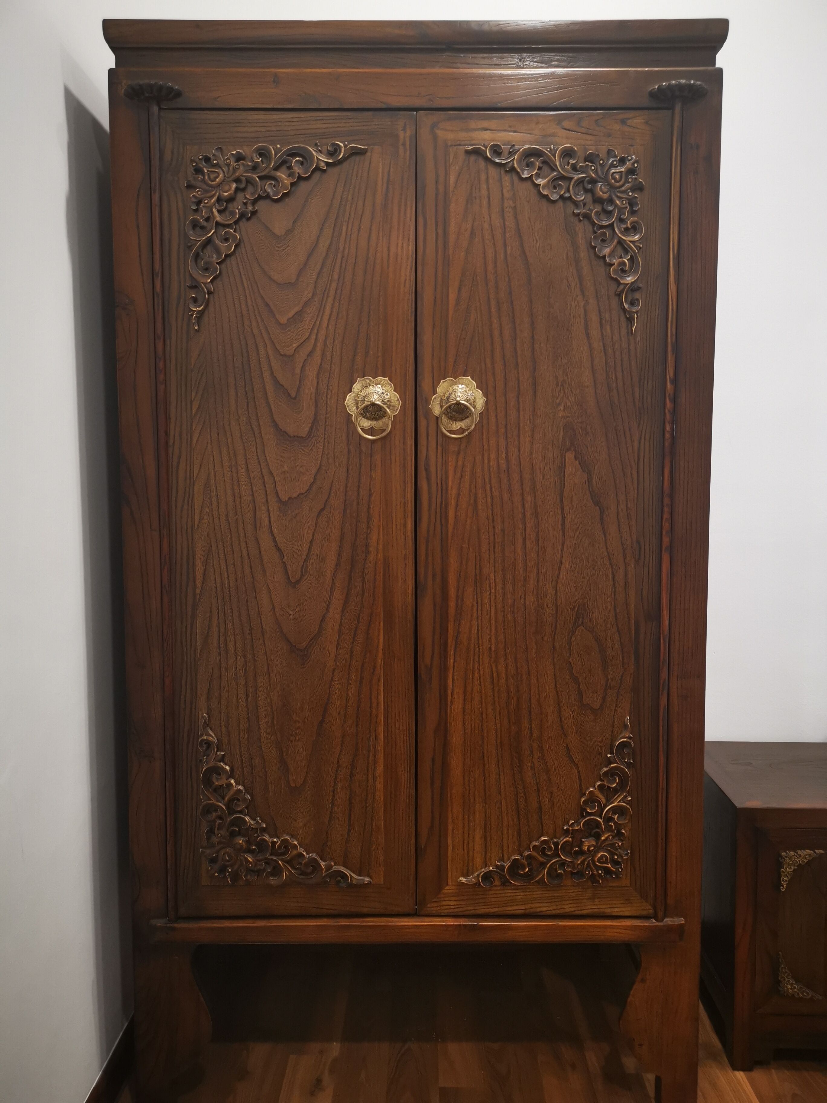 A wooden wardrobe with two doors, each featuring ornate metal handles and decorative carvings.