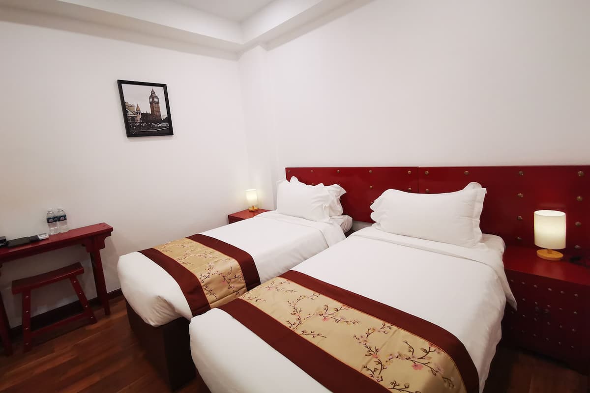 Ein Hotelzimmer mit zwei Betten, einem Nachttisch mit Lampe, einem kleinen Tisch mit Wasserflaschen und einem gerahmten Bild an der Wand.