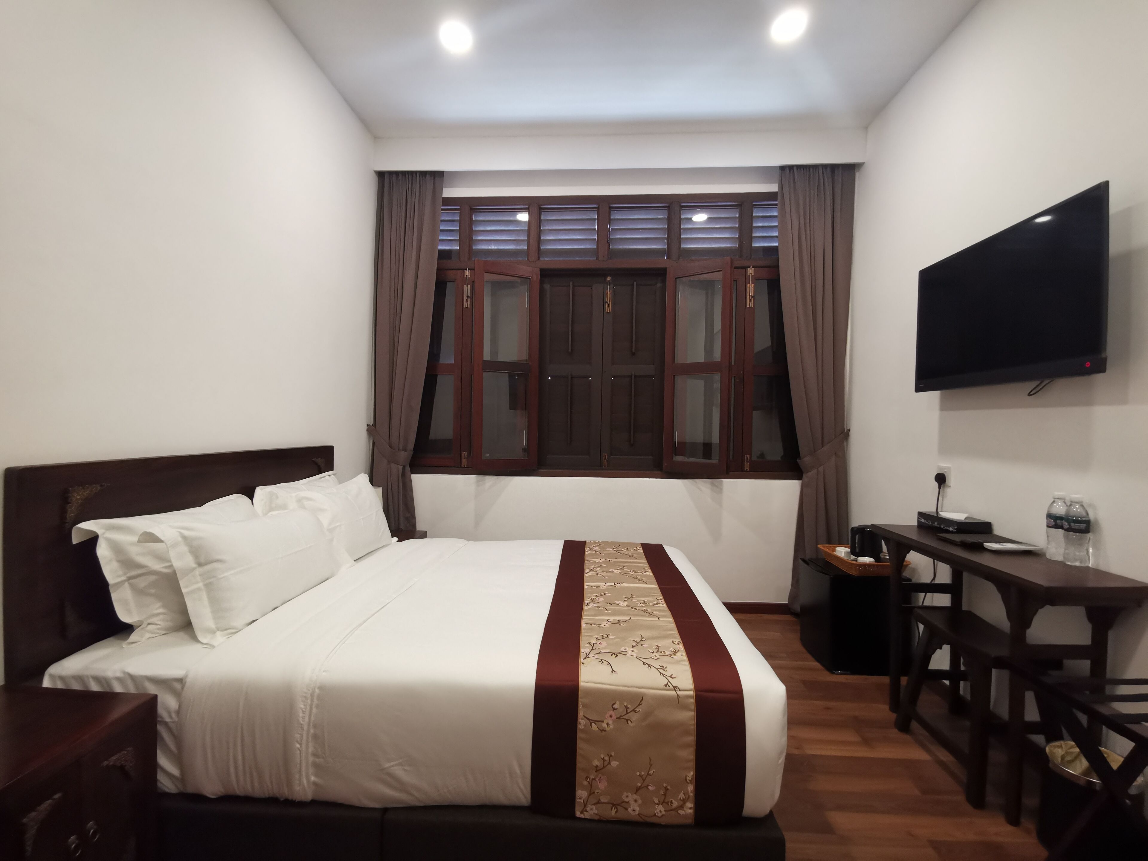 A hotel room with a bed, a desk with a chair, a TV, and a window with curtains.