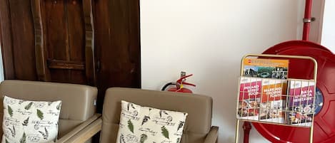 Una habitación con dos sillones beige, cada uno con un cojín estampado, y un extintor rojo montado en la pared.