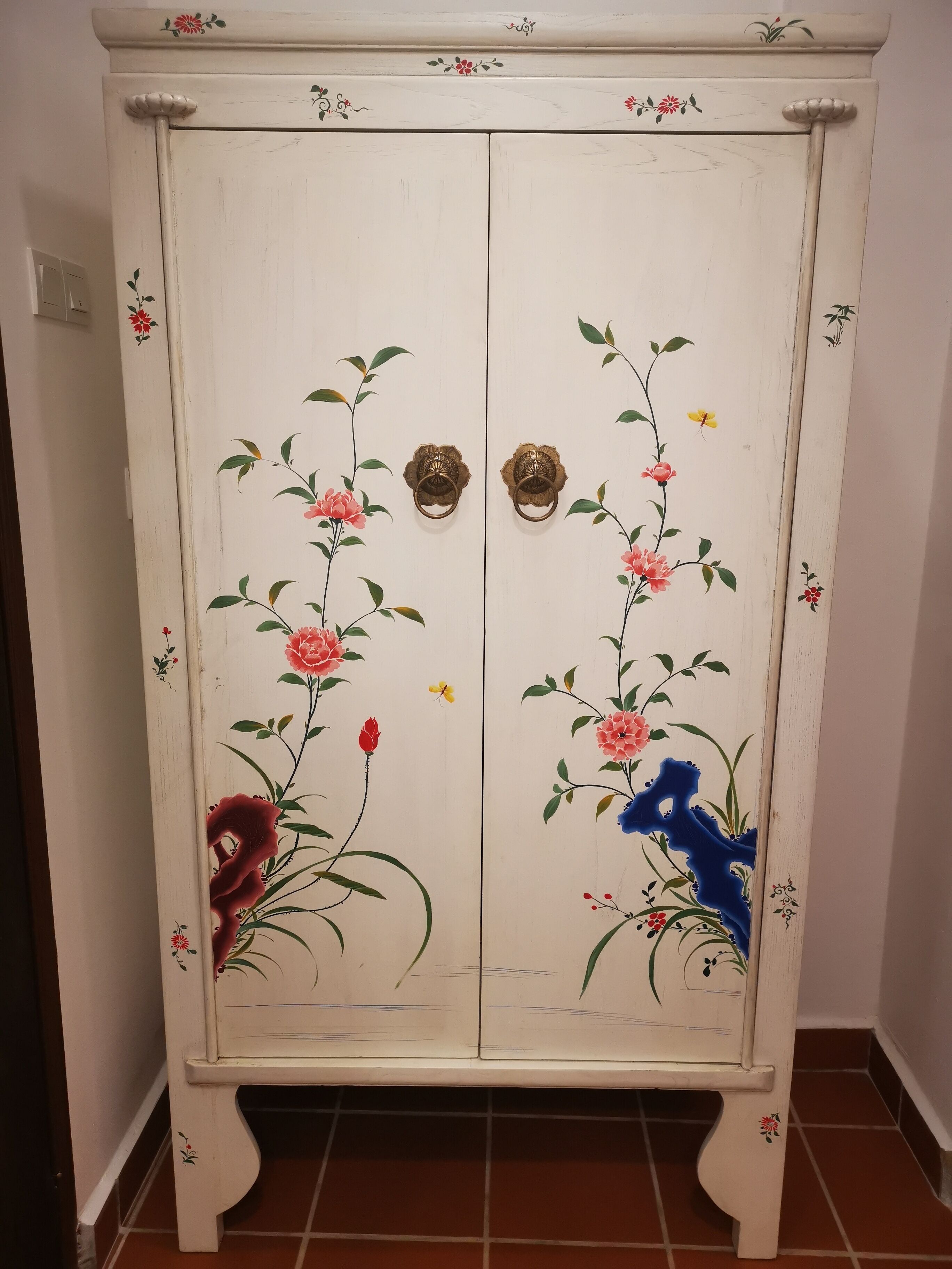 A white cabinet with floral designs and two brass handles.
