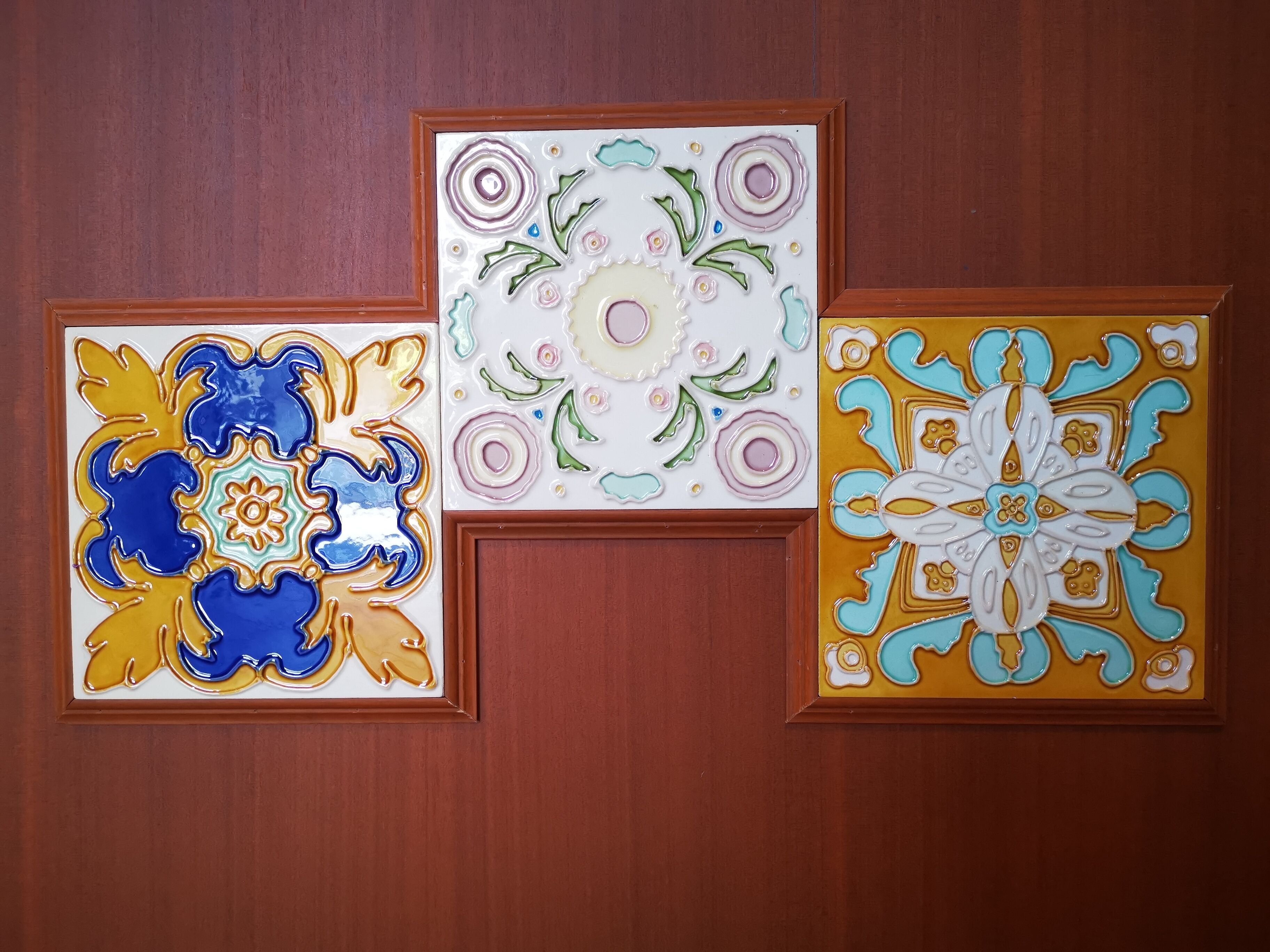 Three framed decorative tiles on a wooden wall.