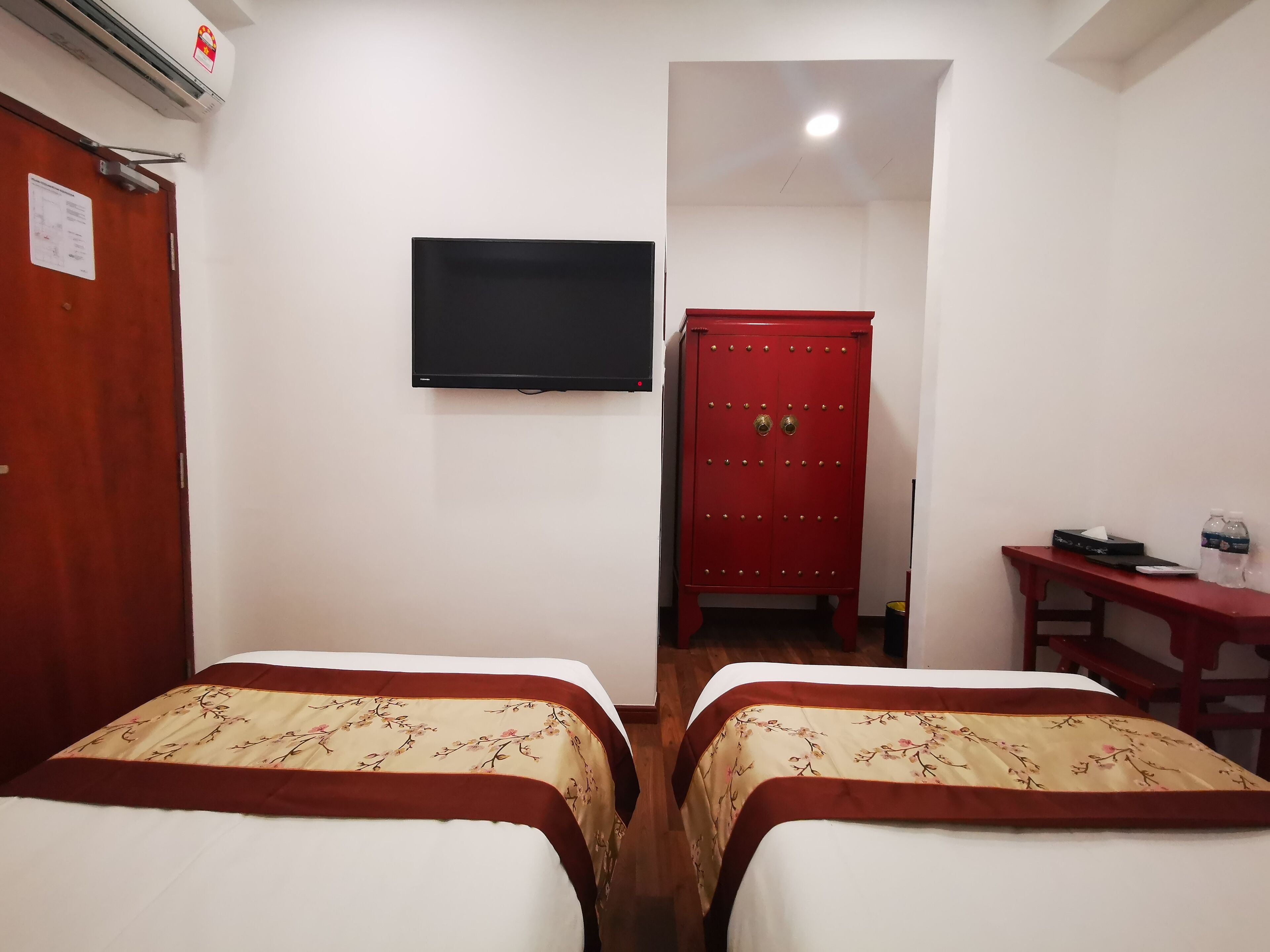 A hotel room with two beds, a TV, a red cabinet, and a small table with a water bottle.