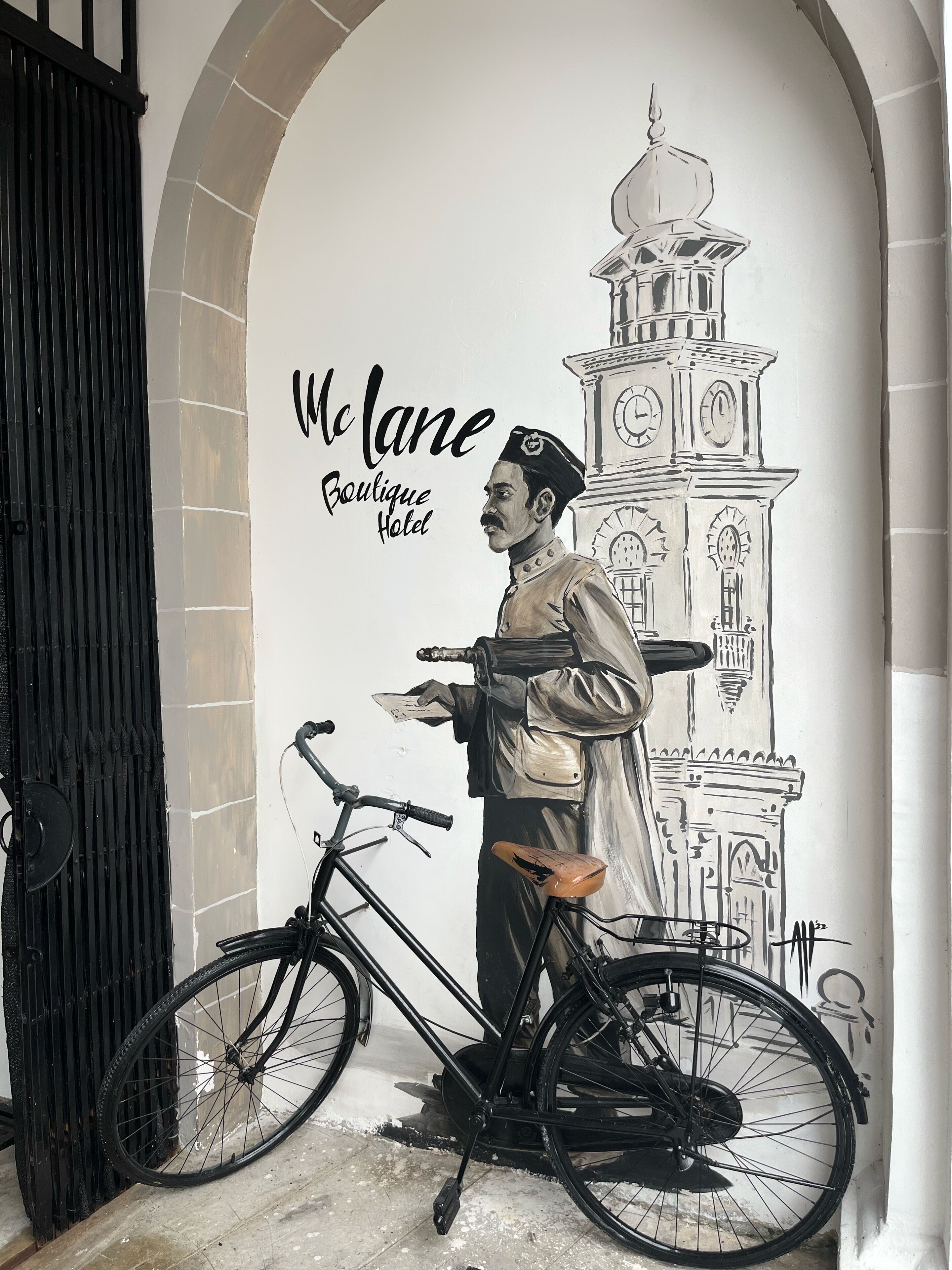 A mural of a man with a bicycle and a clock tower, labeled "McLane Boutique Hotel".