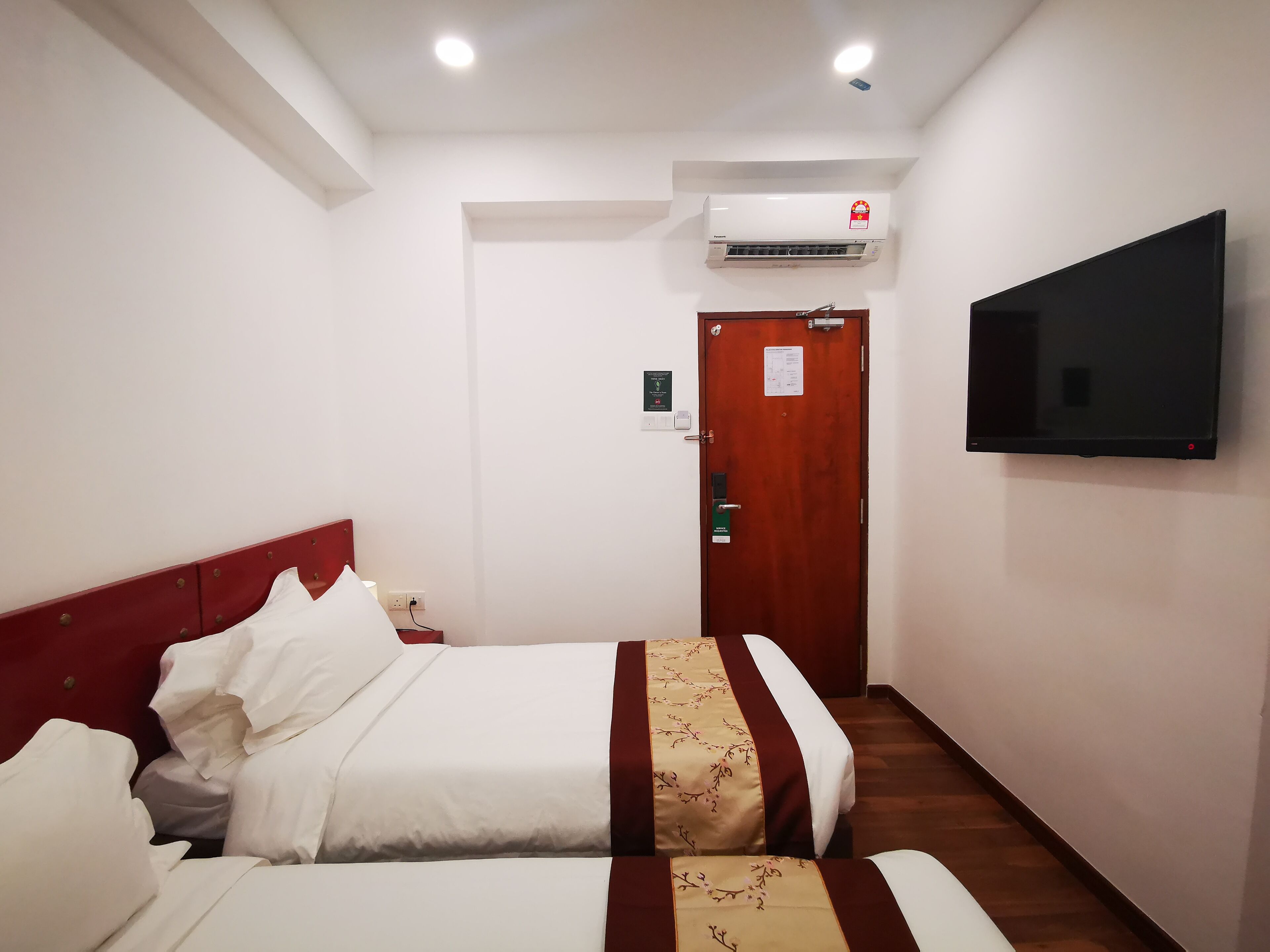 A hotel room with a bed, a TV mounted on the wall, and an air conditioning unit above the door.