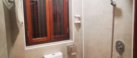 A bathroom with a toilet, a shower, and a window.