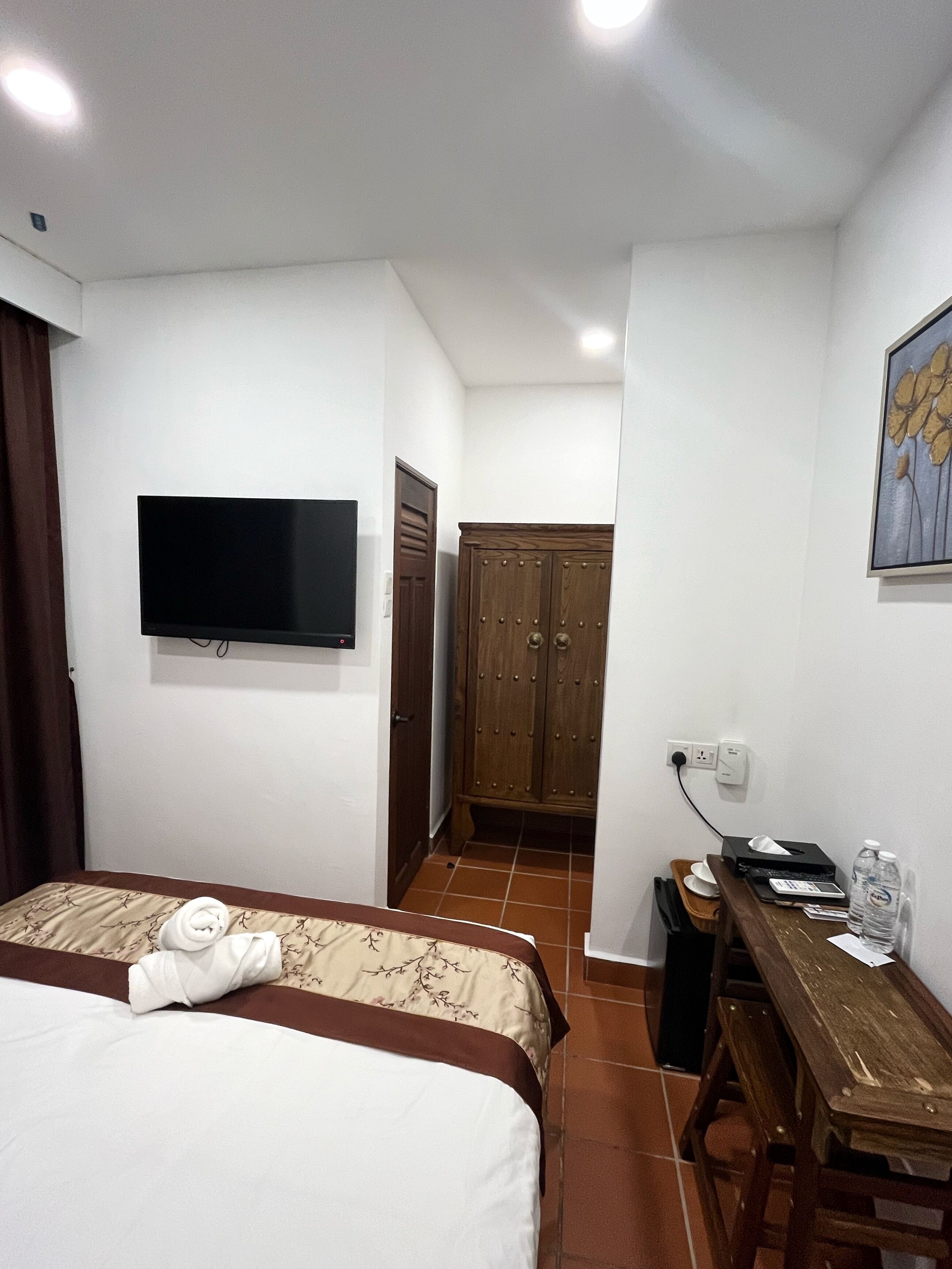 A hotel room with a bed, a desk, a television, a wardrobe, and a painting on the wall.