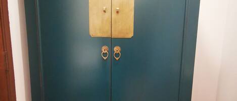 Un mueble color turquesa con dos puertas y un panel central, que incluye tiradores de latón y un cerrojo.