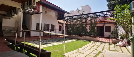 A courtyard with a wooden staircase, a small lawn, and a building with a tiled roof and air conditioning units.