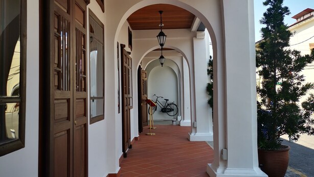 A corridor with wooden doors, a tiled floor, and a hanging light fixture. - Mclane Boutique Hotel (George Town)
