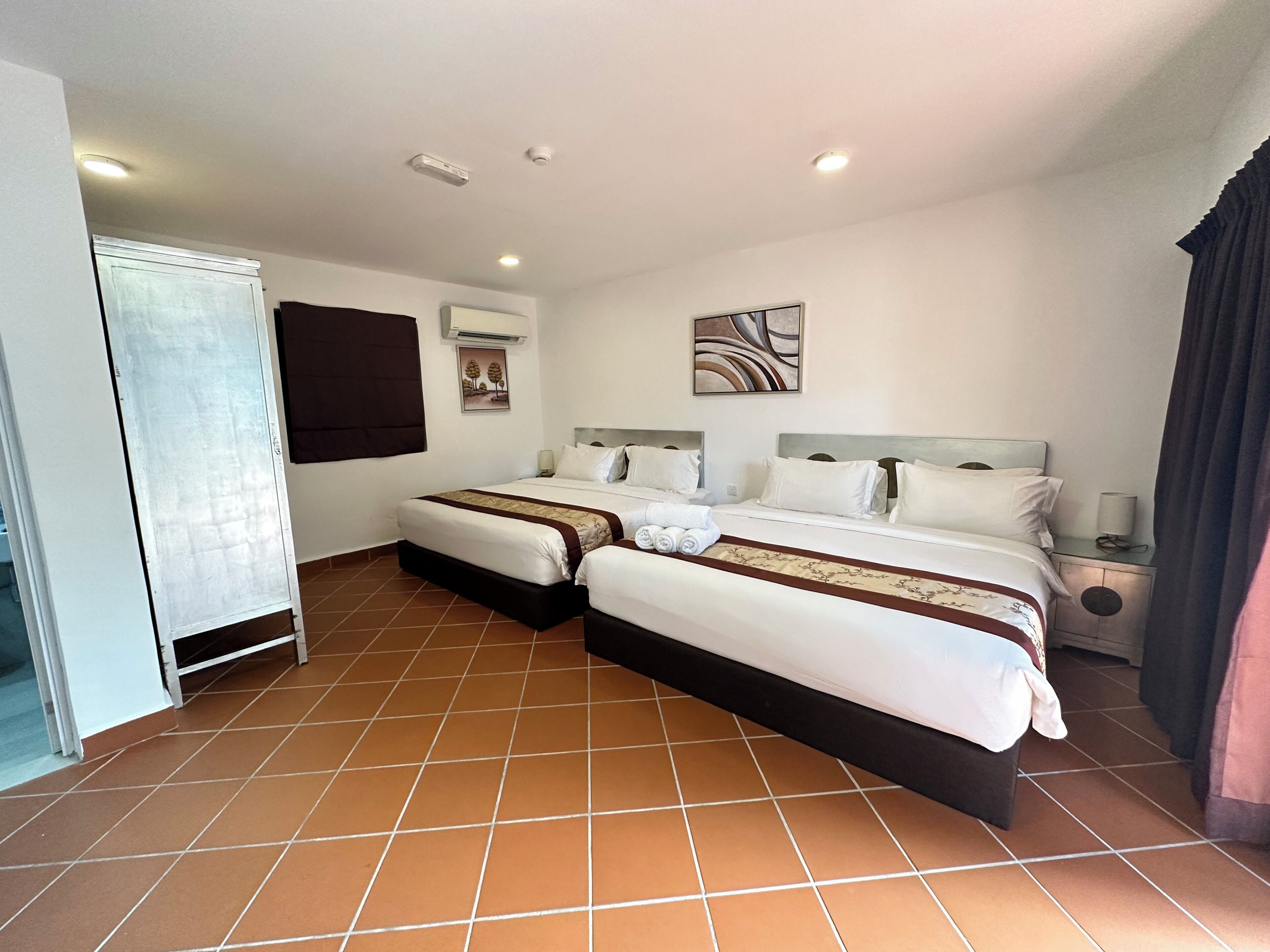 Habitación de hotel con dos camas, un armario, un cuadro y una lámpara en el techo.