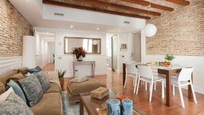 A spacious living area with a modern kitchen, a dining table with white chairs, and a cozy seating area with a brown sofa and patterned cushions. - Enjoybcn Dali Apartments (Barcelona)