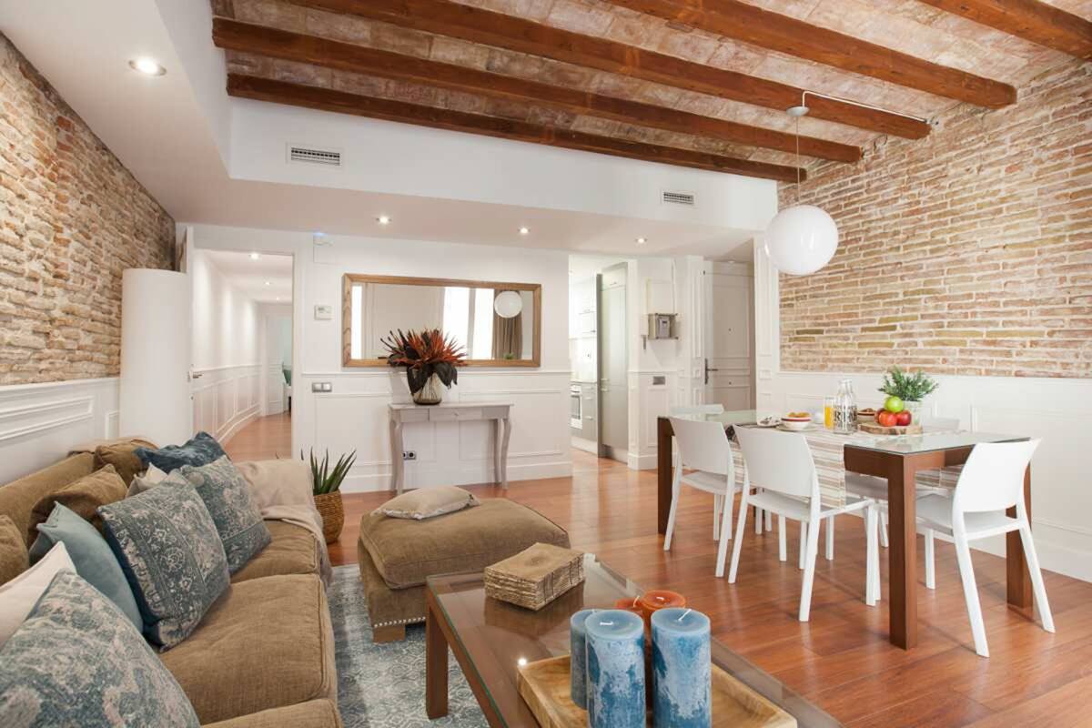 Amplia sala de estar con cocina moderna, mesa de comedor con sillas blancas y un rincón de descanso acogedor con sofá marrón y cojines estampados.