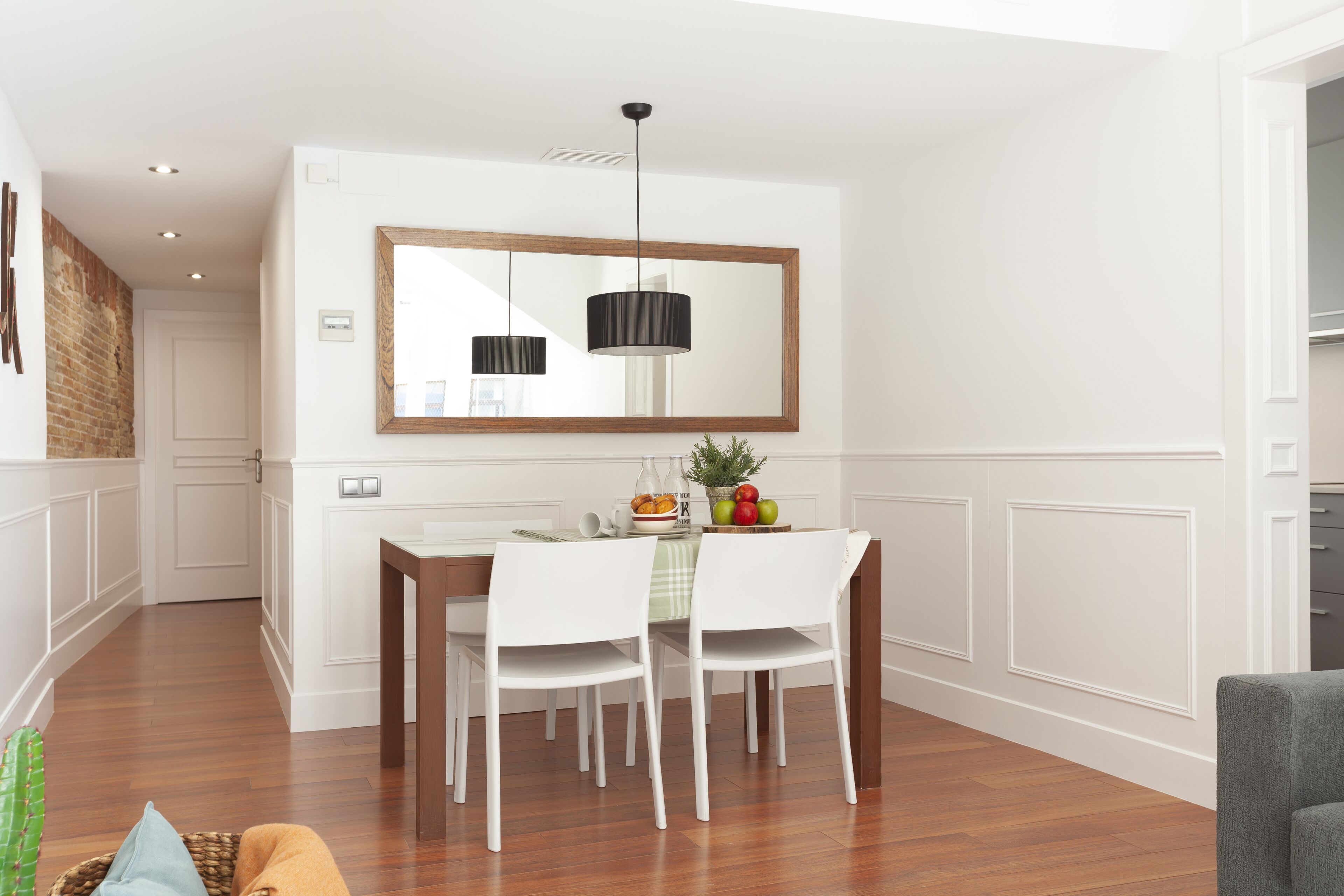 A dining area with a wooden table, white chairs, a mirror above, and a hanging light fixture.