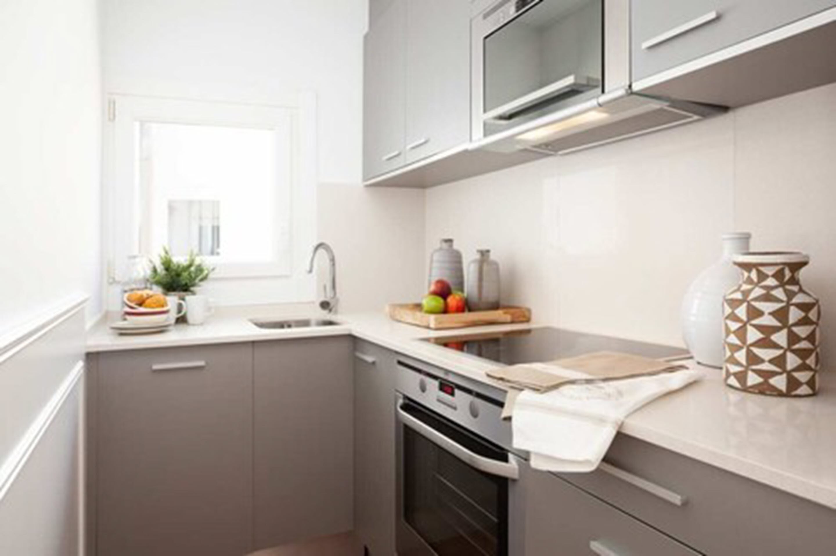 Una cocina moderna con horno integrado, microondas y ventana que deja entrar luz natural.