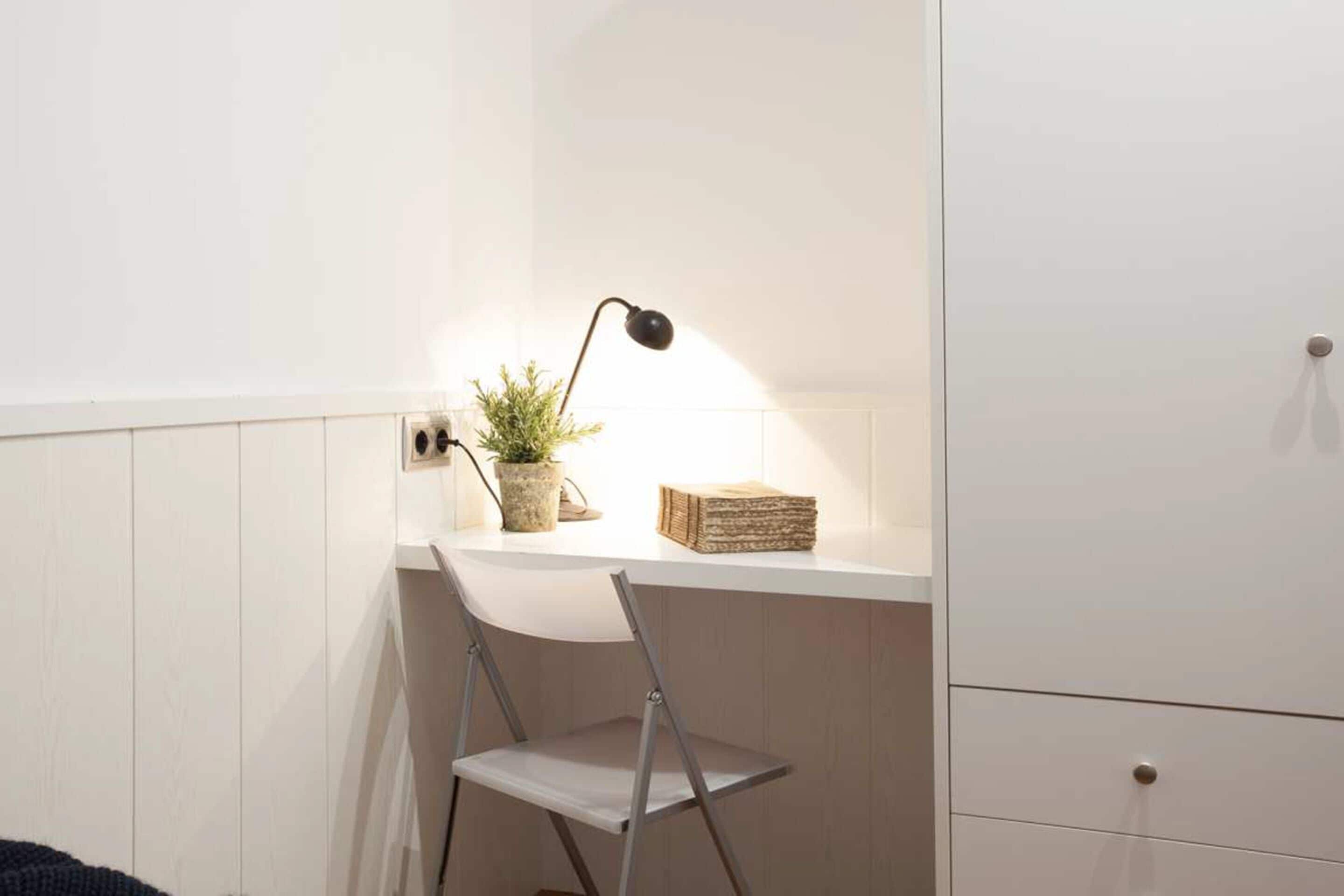 Un bureau blanc avec une lampe, une plante en pot et une pile de livres.