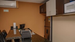 A kitchenette with a microwave, refrigerator, coffee maker, and a sign on the wall.