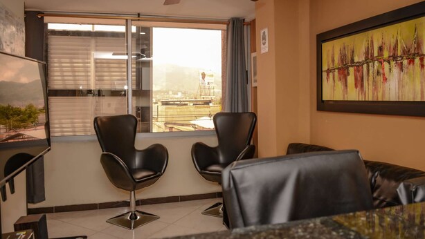 A modern room with two black leather chairs, a ceiling fan, a large window with blinds, and a framed abstract painting on the wall.