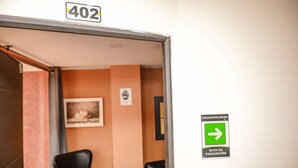 A hotel room entrance with a door labeled '402', a black chair, a framed picture on the wall, and an evacuation route sign.