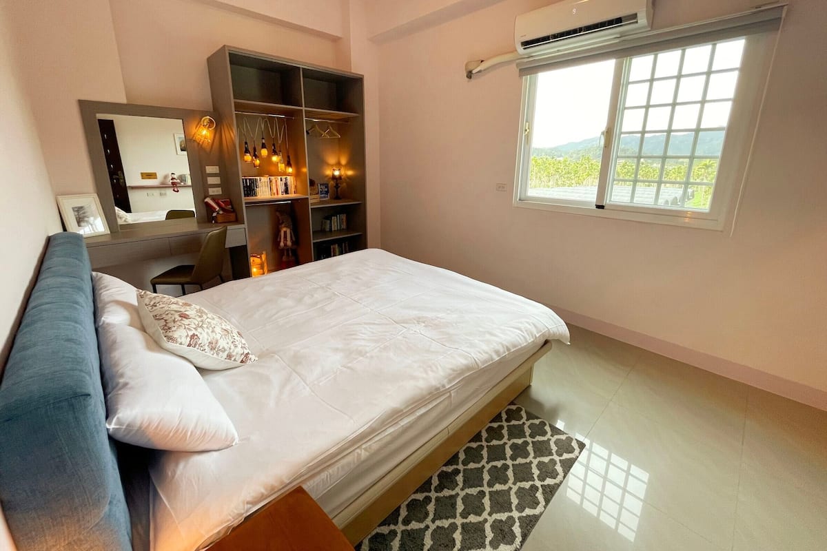 Een slaapkamer met een bed, een kledingkast, een bureau en een raam met uitzicht.